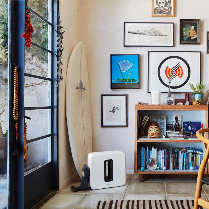 This subwoofer by Sonos is placed beside a bookshelf, demonstrating its flexible placement